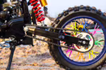 Roda traseira de motocross com raios coloridos e transmissão por corrente.