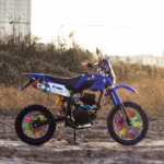 Moto de trilha azul com raios de roda coloridos ao ar livre