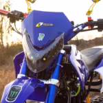 Motocicleta de motocross azul, vista frontal, com adesivos da Monster Energy.