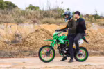Dos ciclistas en una moto de cross verde con radios de colores.