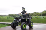 Rider on black ATV with green rims on wooden platform