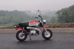 Mini motocicleta vermelha e branca estacionada no asfalto molhado.