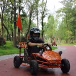 Person driving orange go-kart with spider web design on park path