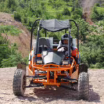 Child driving orange off-road go-kart on dirt terrain