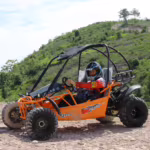 Orange off-road go-kart with driver on rocky terrain